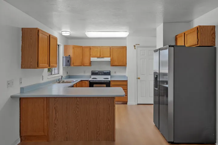 Wood-finish flooring throughout, light wood-toned cabinetry, light-toned countertops, and a built-in range with an overhead microwave