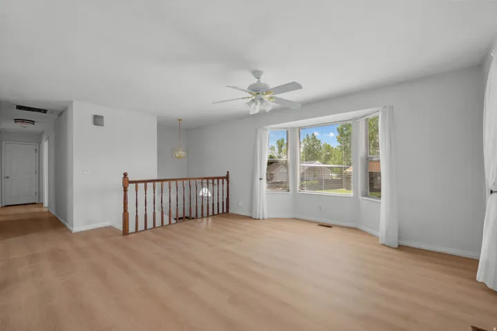 Wood-finish flooring throughout, bay window with multiple panes, ceiling fan, and wooden railing
