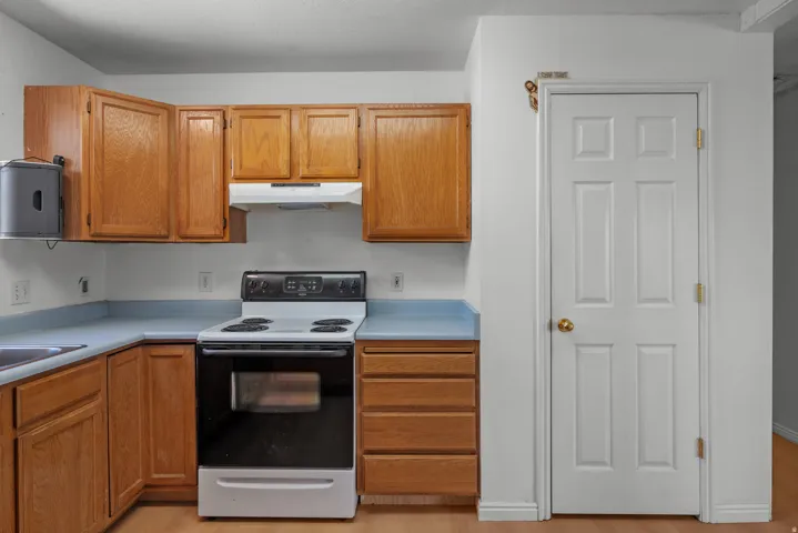 Wood-finish cabinetry, light blue countertops, built-in range hood, and a white six-panel door