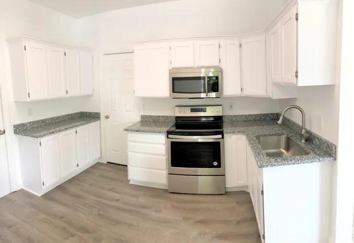 White cabinetry with brushed nickel hardware, gray granite-look countertops, stainless steel appliances, and wood-finish flooring