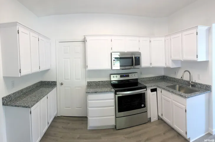 White cabinetry, stainless steel appliances, granite countertops, and wood-finish flooring