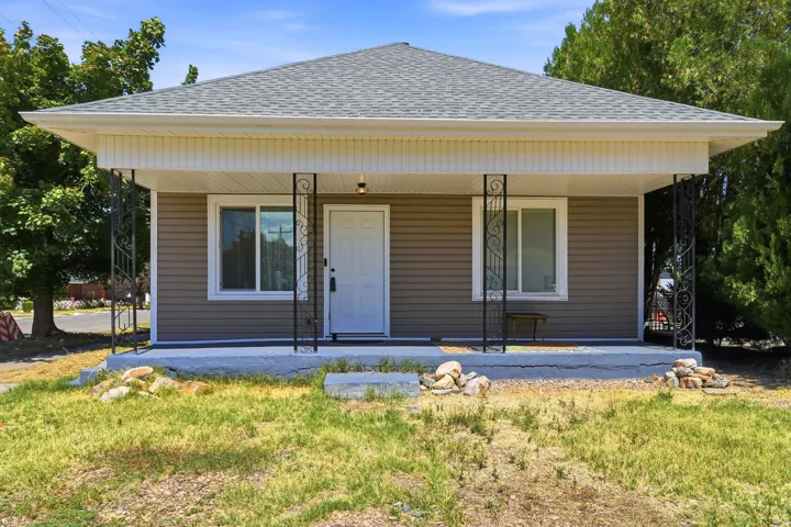 Charming single-story home featuring a wide front porch with decorative columns and metal railings, horizontal vinyl siding with cream and taupe tones, and a pitched roof with dimensional asphalt shingles