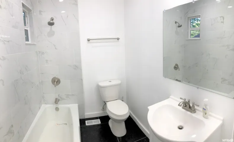 Bathroom featuring a white vanity with an integrated sink, brushed nickel fixtures, a toilet, a bathtub, and white wall tiling