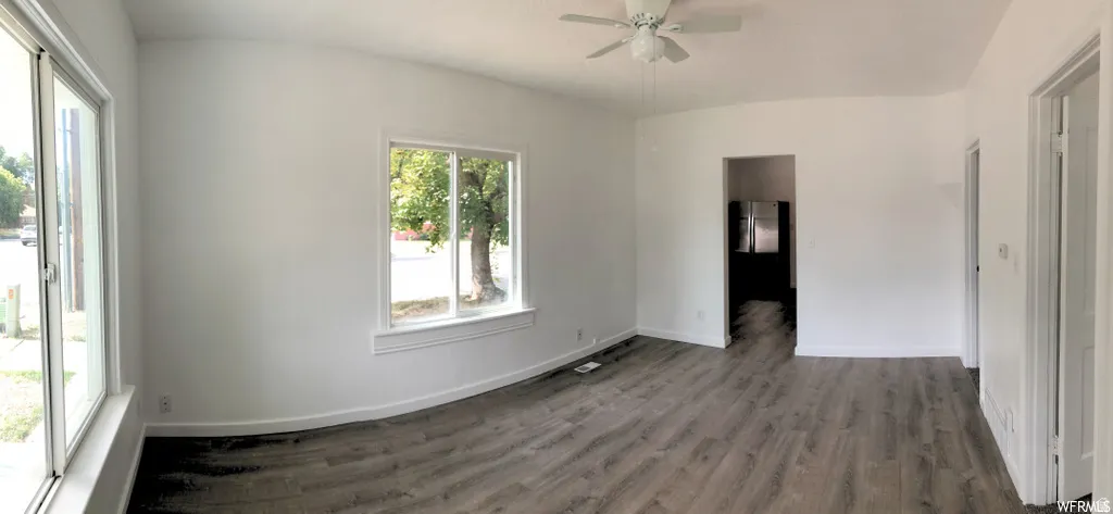 Wood-finish flooring, white walls, white ceiling fan, multiple windows with white trim, and a doorway leading to a separate area