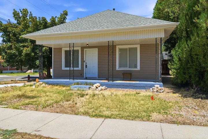 Covered front porch with decorative iron columns, light brown siding, white window trim, and a light gray shingle roof