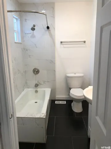 Bathtub with white marble-look subway tile surround, black tile flooring, and white pedestal sink