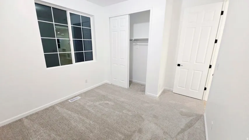 Neutral-toned carpeting, white walls, large multi-pane window, bi-fold closet, and a six-panel door