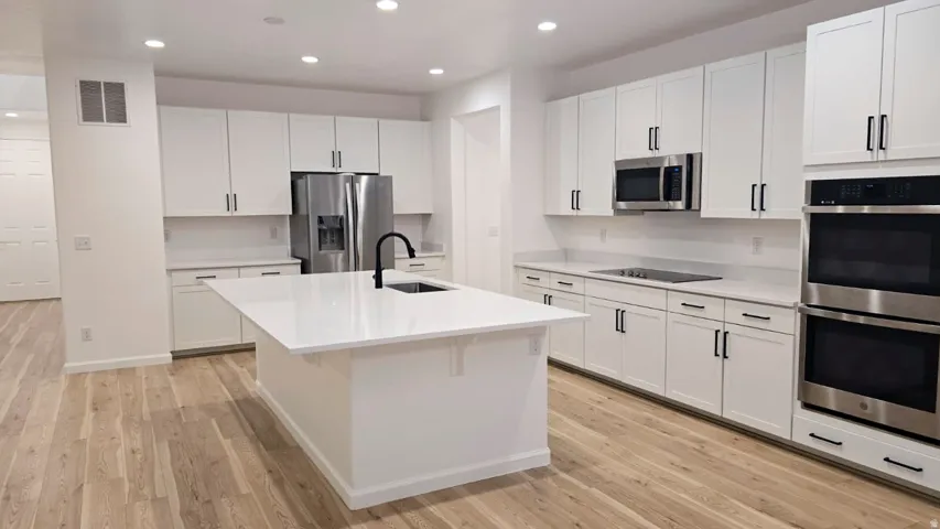 Kitchen featuring white flat-panel cabinetry, a central island with an undermount sink, stainless steel appliances, light-toned wood-finish flooring, and recessed lighting