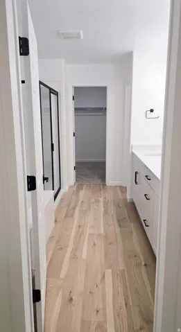Wood-finish flooring, white vanity with black hardware, white countertop, and a shower with black frame enclosure