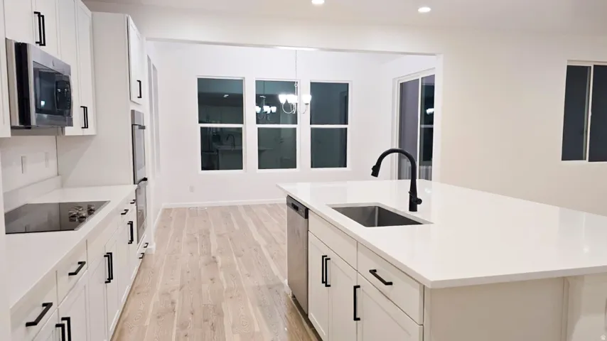 Kitchen featuring an expansive island with an undermount sink and a matte black gooseneck faucet, white cabinetry with black hardware, integrated stainless steel appliances, and wood-finish flooring