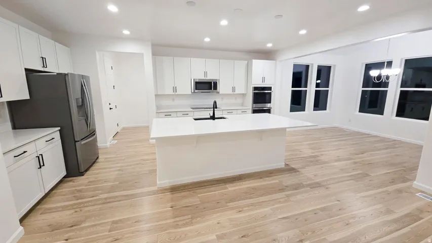 Open-concept kitchen featuring white cabinetry, stainless steel appliances, a center island with sink, recessed lighting, and wood-finish flooring