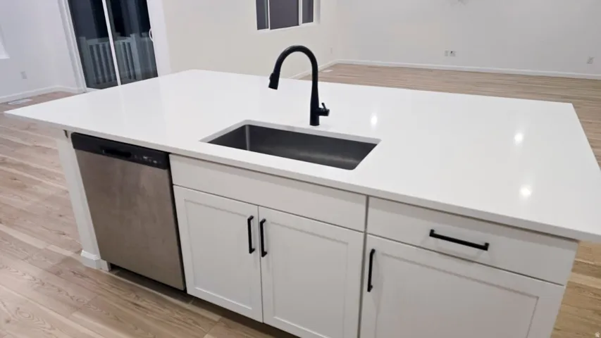 Kitchen island with a white countertop, undermount sink with a matte black faucet, integrated dishwasher, and white shaker-style cabinetry with matte black hardware
