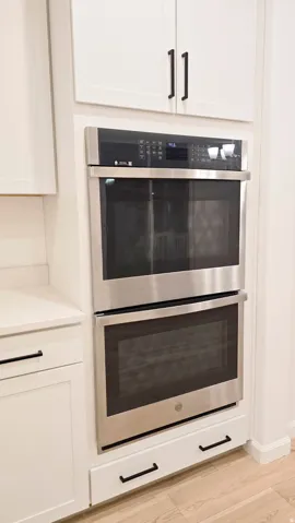 Stainless steel double oven integrated into white cabinetry with black hardware
