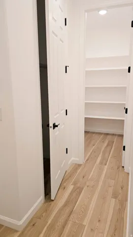 Wood-finish flooring leading to a built-in shelving unit, featuring white paneled doors with matte black hardware