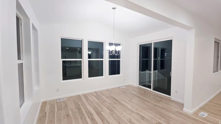 Vaulted ceiling with a contemporary chandelier, multiple windows, large sliding glass door, and wood-finish flooring