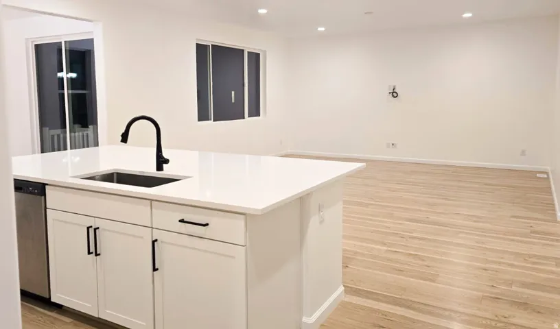 Kitchen island with a stainless steel sink, black faucet, and white cabinetry