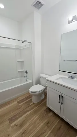 White cabinetry with black hardware, integrated sink, wood-finish flooring, and a white tub with shower