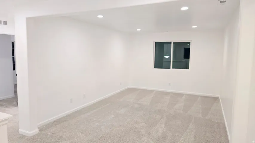 Recessed lighting illuminates this room featuring light-toned carpeting and a window