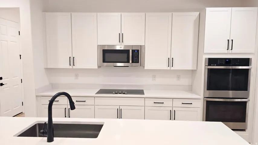 White cabinetry with matte black hardware, stainless steel appliances, built-in microwave, and a black gooseneck faucet
