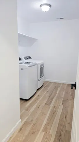 Laundry area featuring wood-finish flooring, a wall-mounted shelf, and an overhead light fixture