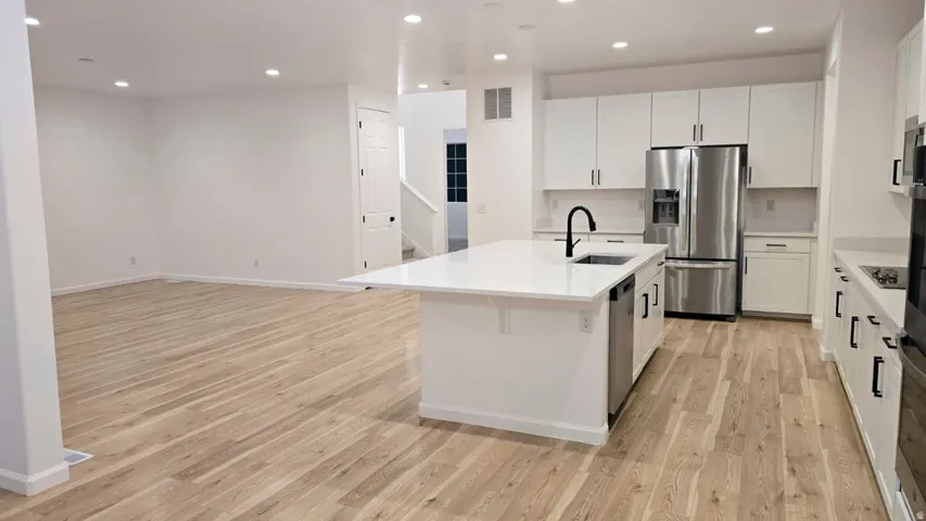 Open-concept living area featuring wood-finish flooring, recessed lighting, a kitchen island with seating, a stainless steel refrigerator, and white cabinetry