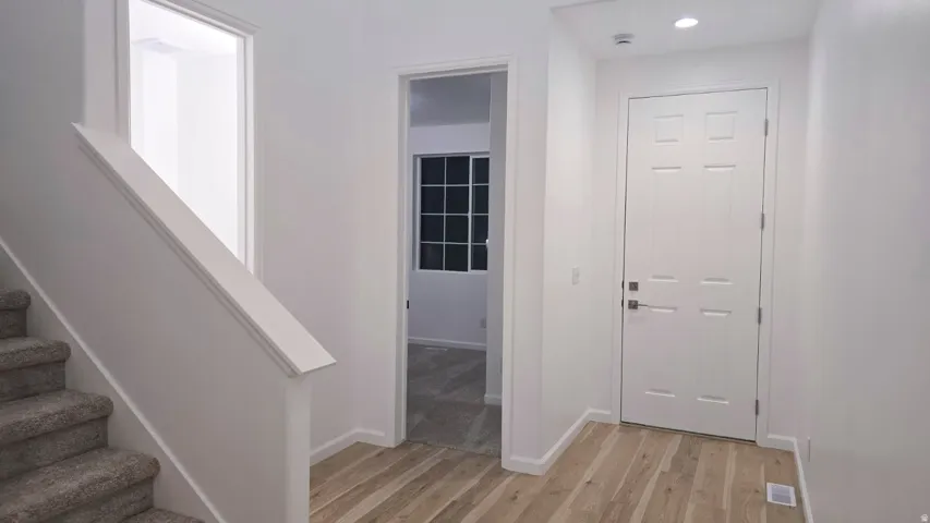 Light wood-finish flooring, white paneled door, recessed lighting, and a staircase with carpeted treads