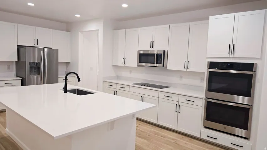 Kitchen featuring white shaker cabinetry, white countertops, a large center island with an undermount sink, stainless steel appliances, and recessed lighting
