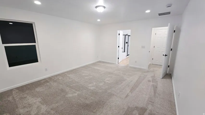 Neutral-toned carpeting throughout, recessed lighting, and a single window with a white frame