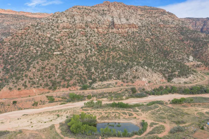 Expansive natural landscape with a prominent mountain backdrop, natural pond, and winding unpaved roads