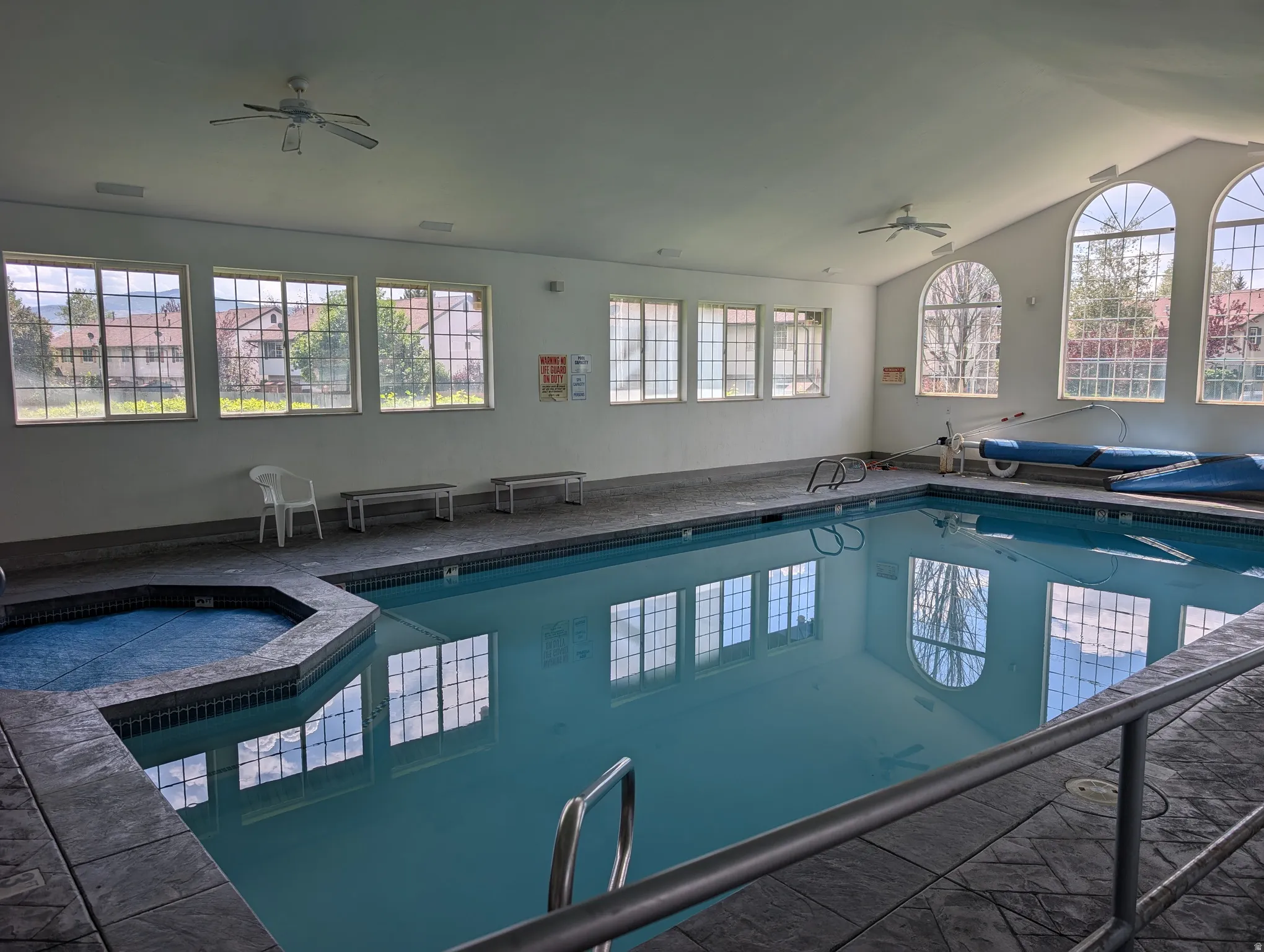 Indoor swimming pool with an attached spa, vaulted ceiling, and multiple windows