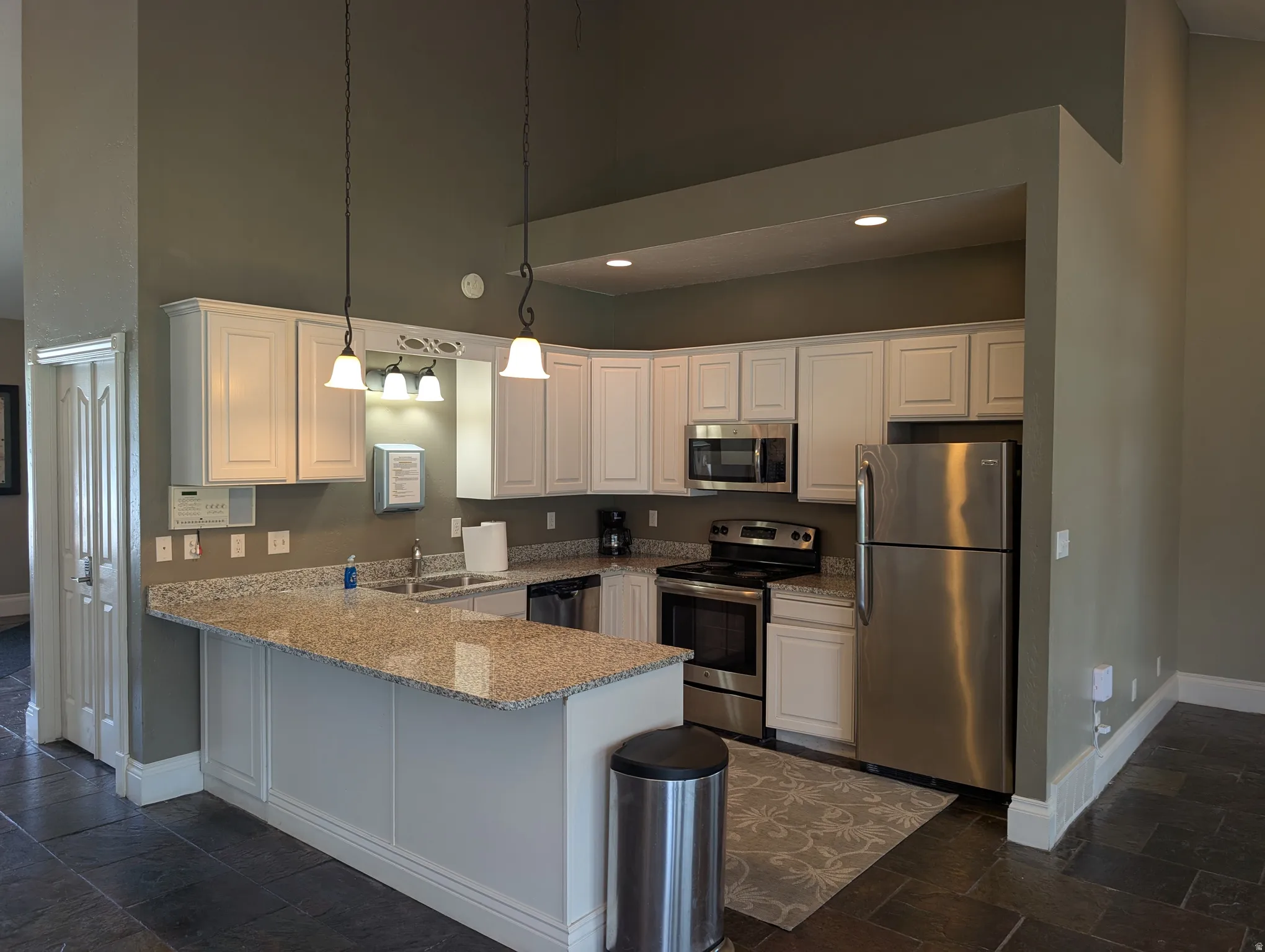 Kitchen featuring white cabinetry, granite countertops, stainless steel appliances, and dark tile flooring
