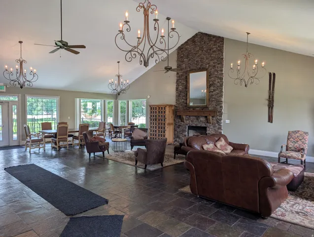 Spacious common area featuring a vaulted ceiling with exposed beams, multiple decorative chandeliers, a stone-clad fireplace with a wood mantle, and large windows