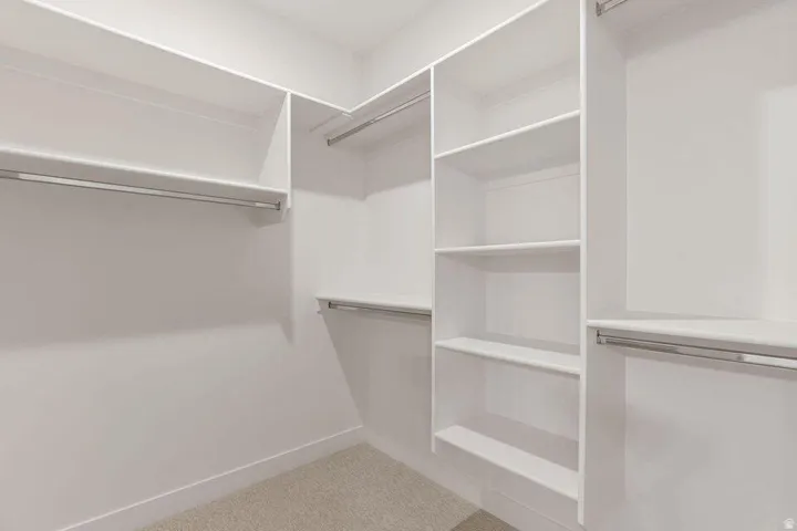 Built-in closet system featuring white shelving, multiple hanging rods, and carpet flooring