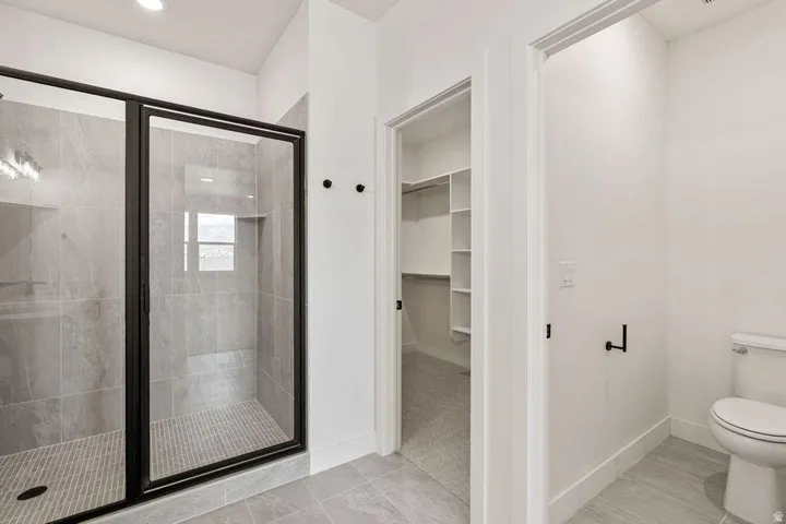 Spacious bathroom featuring a glass-enclosed shower with tiled walls and floor, a separate water closet, and a walk-in closet with built-in shelving