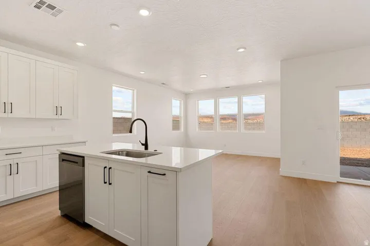 Open-concept design featuring wood-finish flooring, white cabinetry, recessed lighting, and a kitchen island with an undermount sink and matte black faucet