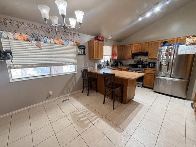 Kitchen area featuring a tiled floor, wood cabinetry, stainless steel appliances, and a vaulted ceiling