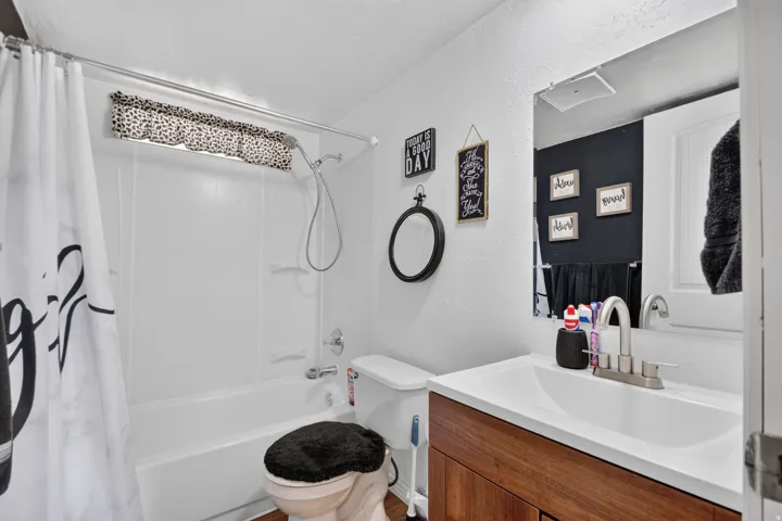 White shower and tub combination, single vanity with wood-finish cabinetry, and an integrated white sink