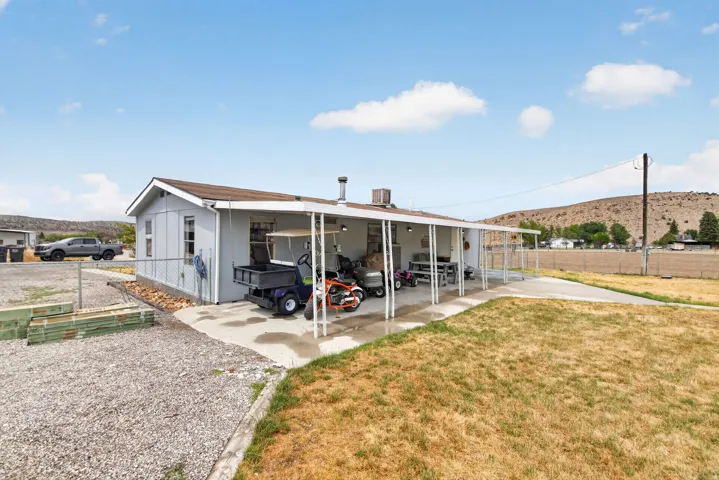 Property exterior with a covered patio, gravel driveway, and surrounding landscape