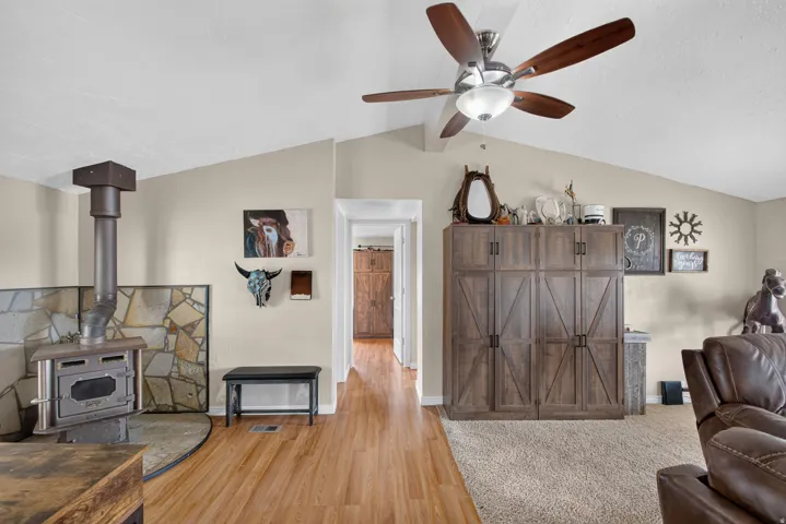 Vaulted ceilings, wood-finish flooring, wood-burning stove with stone surround, ceiling fan, and built-in cabinetry