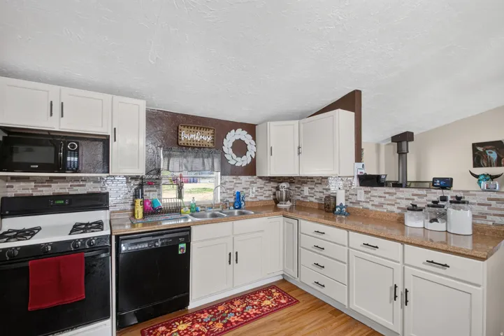 Kitchen featuring white cabinetry with dark hardware, a mosaic tile backsplash, wood-finish flooring, a double basin sink, and a built-in microwave