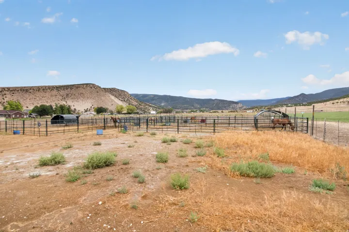 Expansive outdoor paddocks with metal fencing and shelter structures, set against a mountainous backdrop
