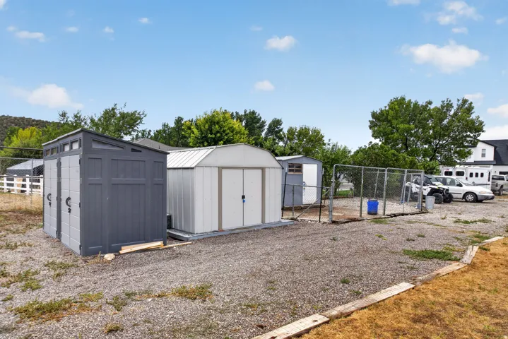 Gravel lot featuring multiple storage sheds, a chain-link fenced area, and a white fence border