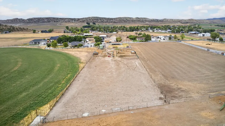 Expansive land offering a large cultivated field, a fenced dirt lot, and distant mountain scenery