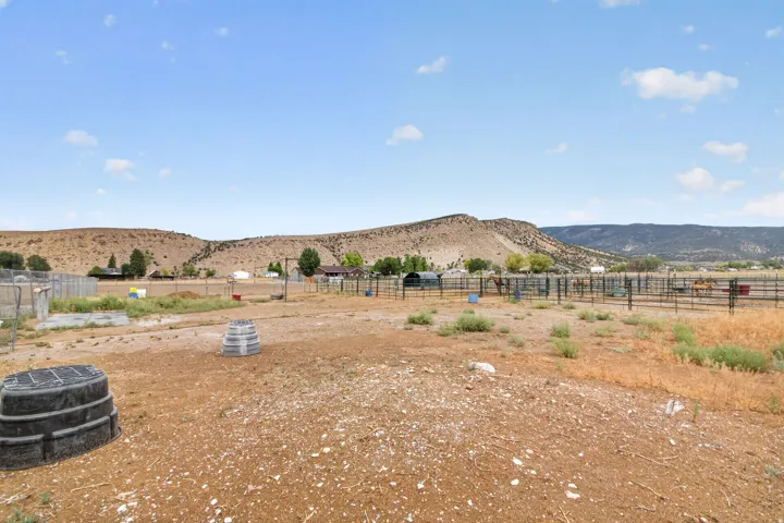 Expansive uncultivated land with natural topography, enclosed by metal fencing, and featuring distant mountain ranges