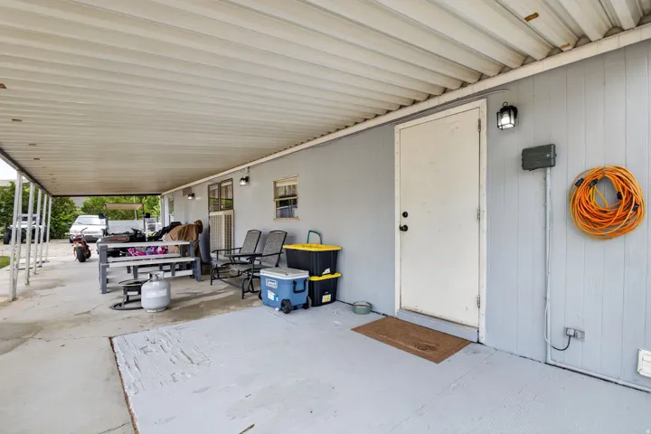 Covered patio with a light gray painted concrete surface, exterior door, and wall-mounted light fixtures