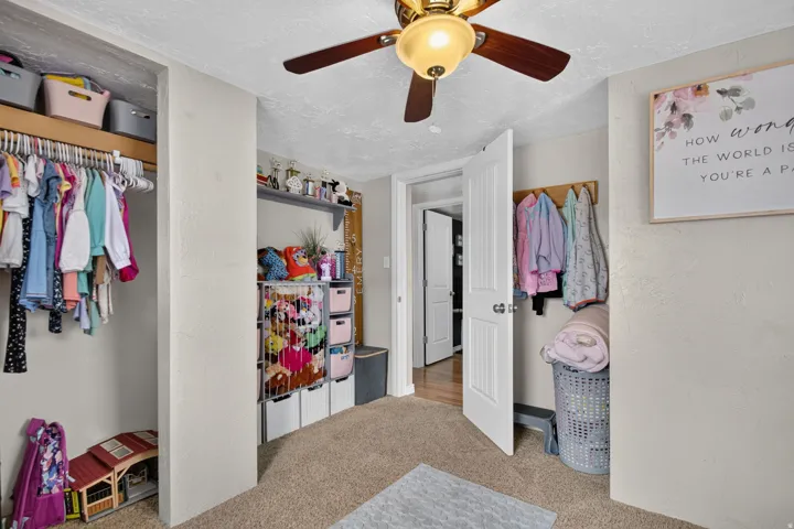 Spacious bedroom with carpeted flooring, ceiling fan with integrated lighting, and built-in closet storage featuring multiple hanging rods, shelving units, and organizational systems