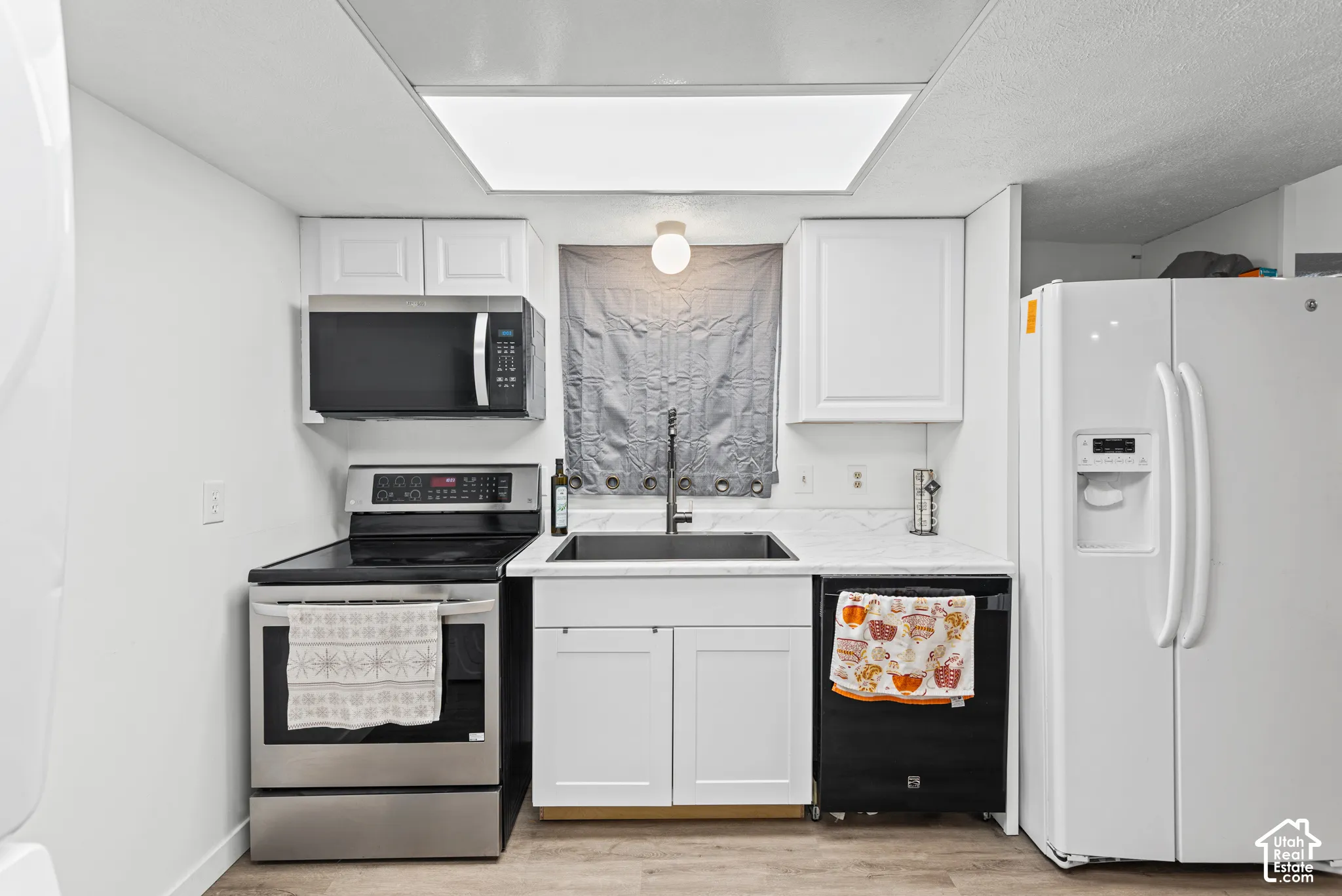 Stainless steel range with an overhead microwave, white cabinetry, integrated sink with a black faucet, white refrigerator, and wood-finish flooring