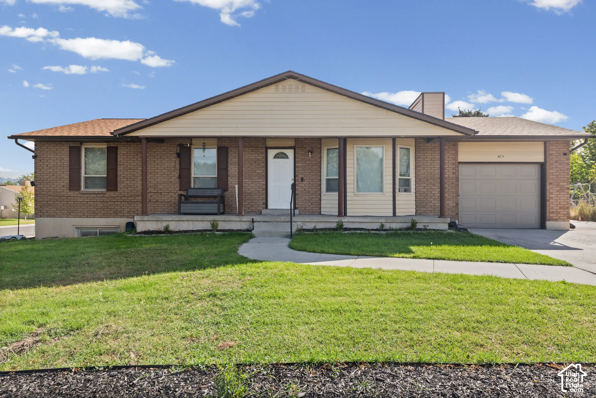 Brick exterior with a covered porch, attached garage, and a front yard with mature landscaping