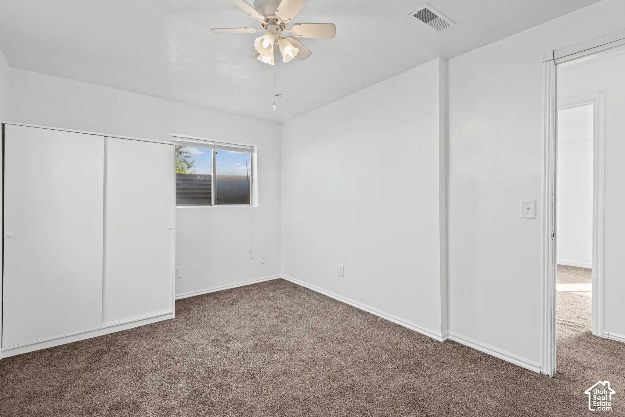 Neutral wall tones with a window, ceiling fan, and carpeted flooring