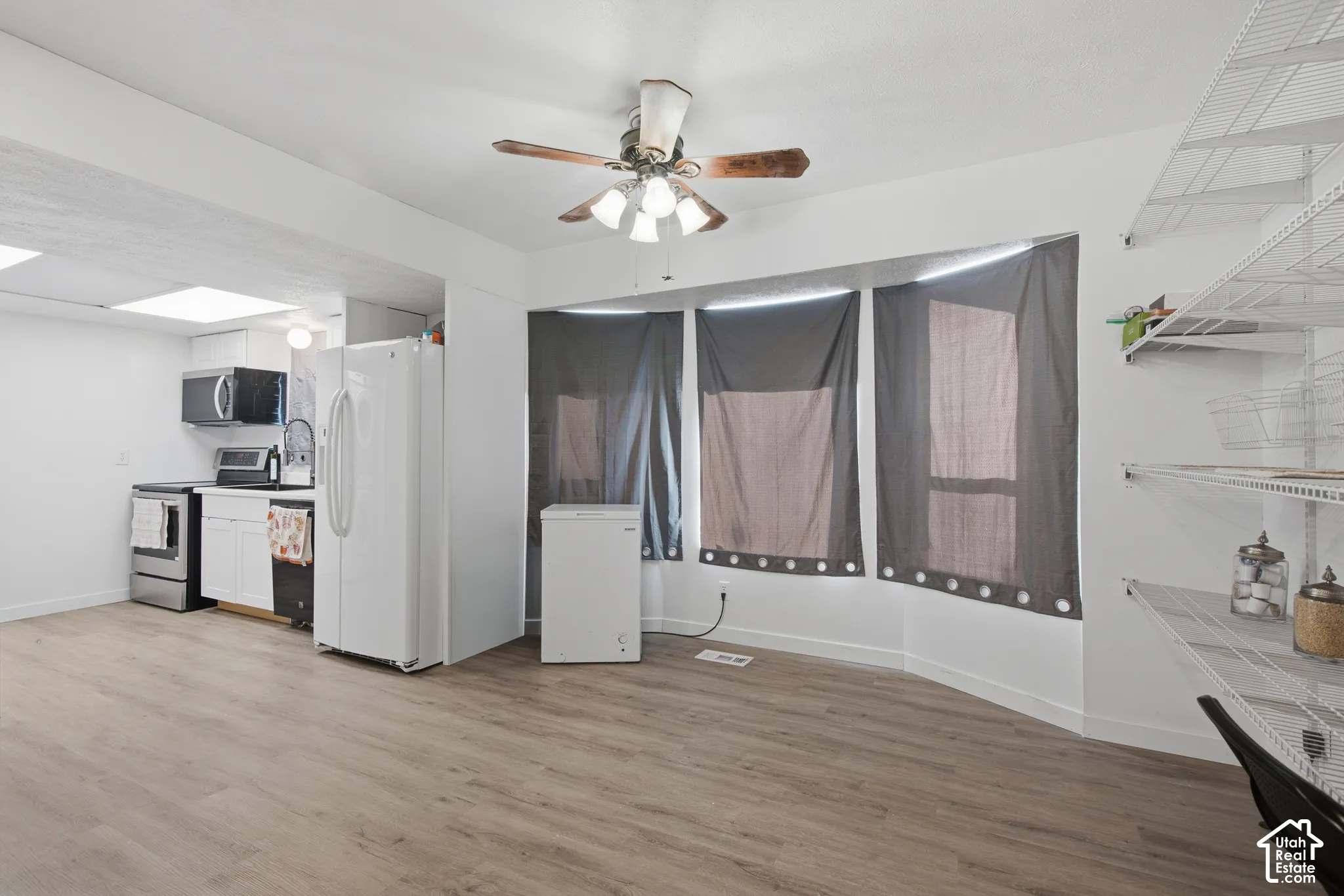Open-concept living space with wood-finish flooring, a ceiling fan, and integrated kitchen appliances
